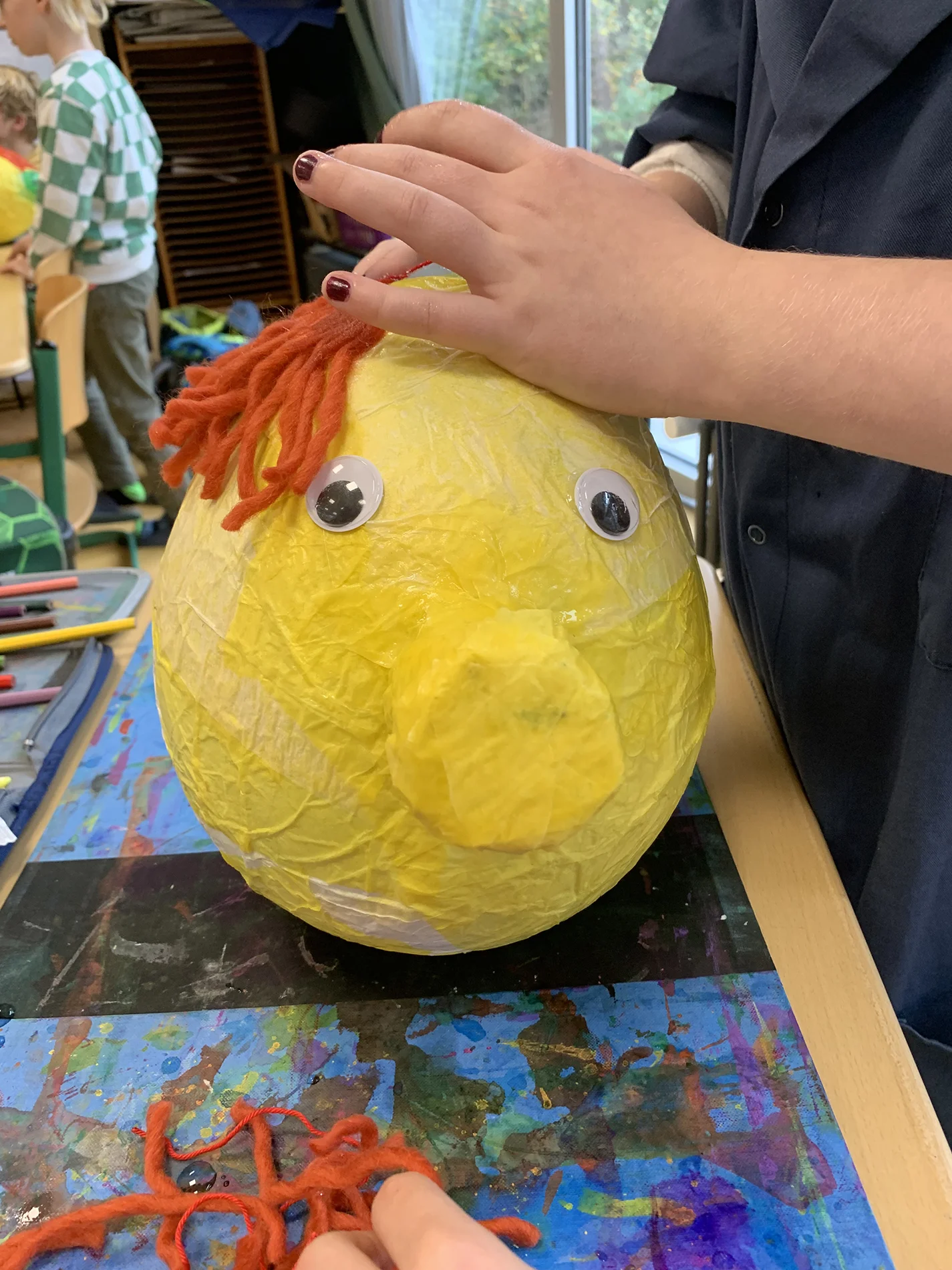 Kind gestaltet eine große gelbe Laterne mit roten Wollhaaren und Wackelaugen. Kind gestaltet eine große gelbe Laterne mit roten Wollhaaren und Wackelaugen.