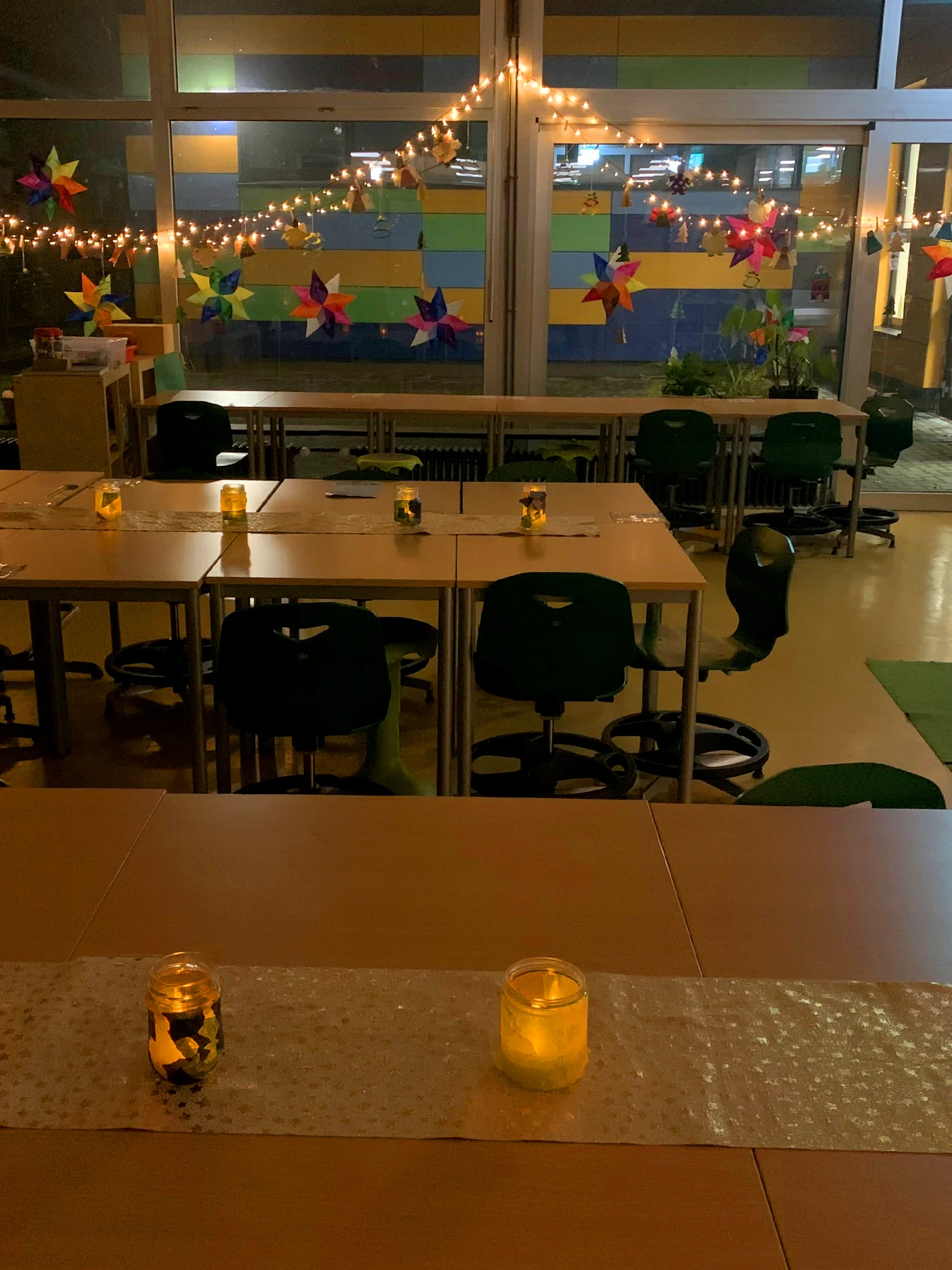 Klassenraum am Abend mit Lichterketten, bunten Papiersternen am Fenster und leuchtenden Windlichtern auf den Tischen Klassenraum am Abend mit Lichterketten, bunten Papiersternen am Fenster und leuchtenden Windlichtern auf den Tischen