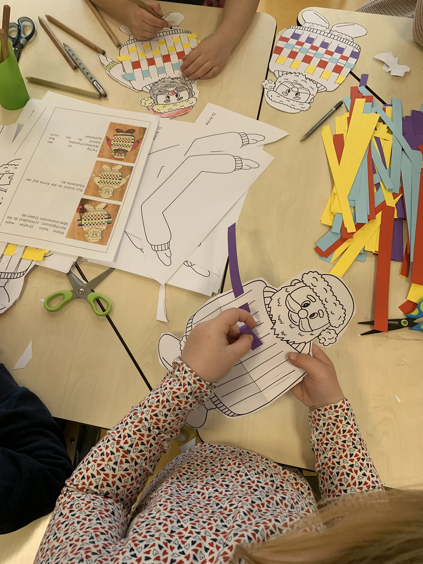 Kinder basteln Figuren aus Papier, in die bunte Streifen eingeflochten werden. Kinder basteln Figuren aus Papier, in die bunte Streifen eingeflochten werden.