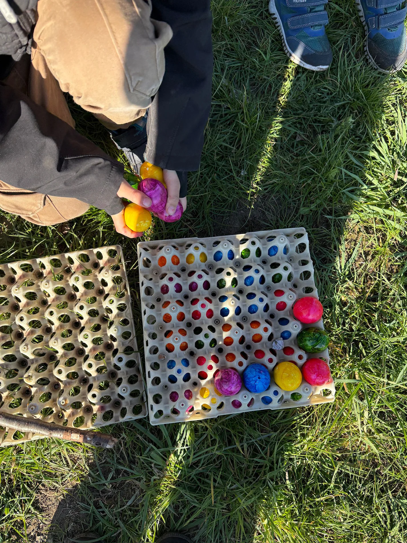 Kind hält bunte Ostereier über einem vollen Eierkarton im Gras. Kind hält bunte Ostereier über einem vollen Eierkarton im Gras.