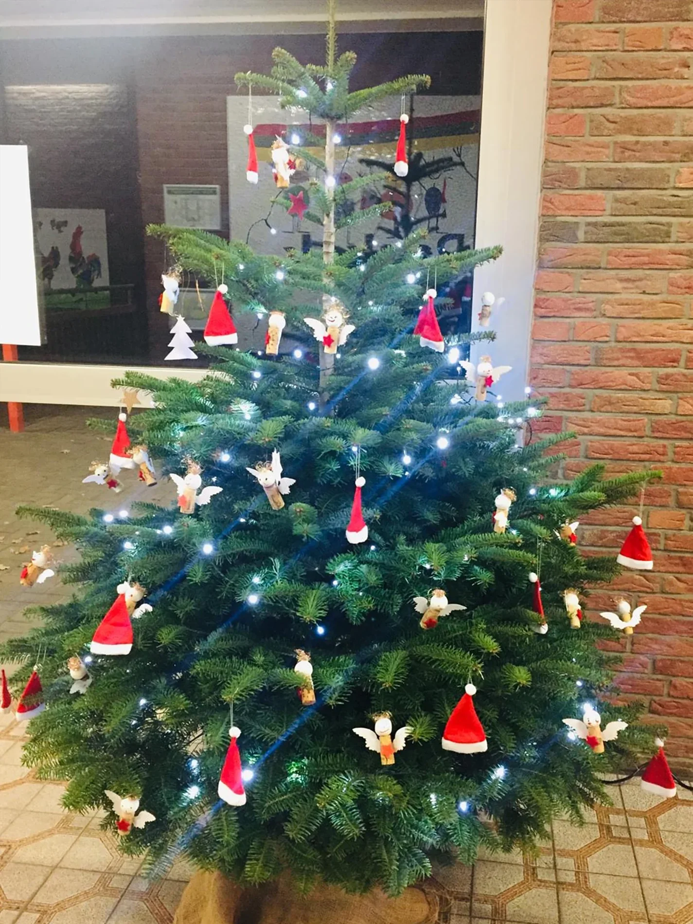 ottopankockschuledrevenack_impressionen9 Weihnachtsbaum mit weißen Lichtern, geschmückt mit kleinen roten Nikolausmützen und gebastelten Engeln