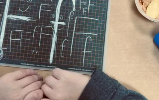 ottopankockschuledrevenack_anfangsunterricht_1 Kind übt auf Schreibtafel das Schreiben des Buchstabens F mit Kreide – erste Schreibübungen im Unterricht.