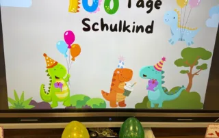 Digitale Tafel zeigt buntes Motiv‚ 100 Tage Schulkind‘ mit Luftballons und fröhlichen Dinosauriern. Digitale Tafel zeigt buntes Motiv‚ 100 Tage Schulkind‘ mit Luftballons und fröhlichen Dinosauriern.