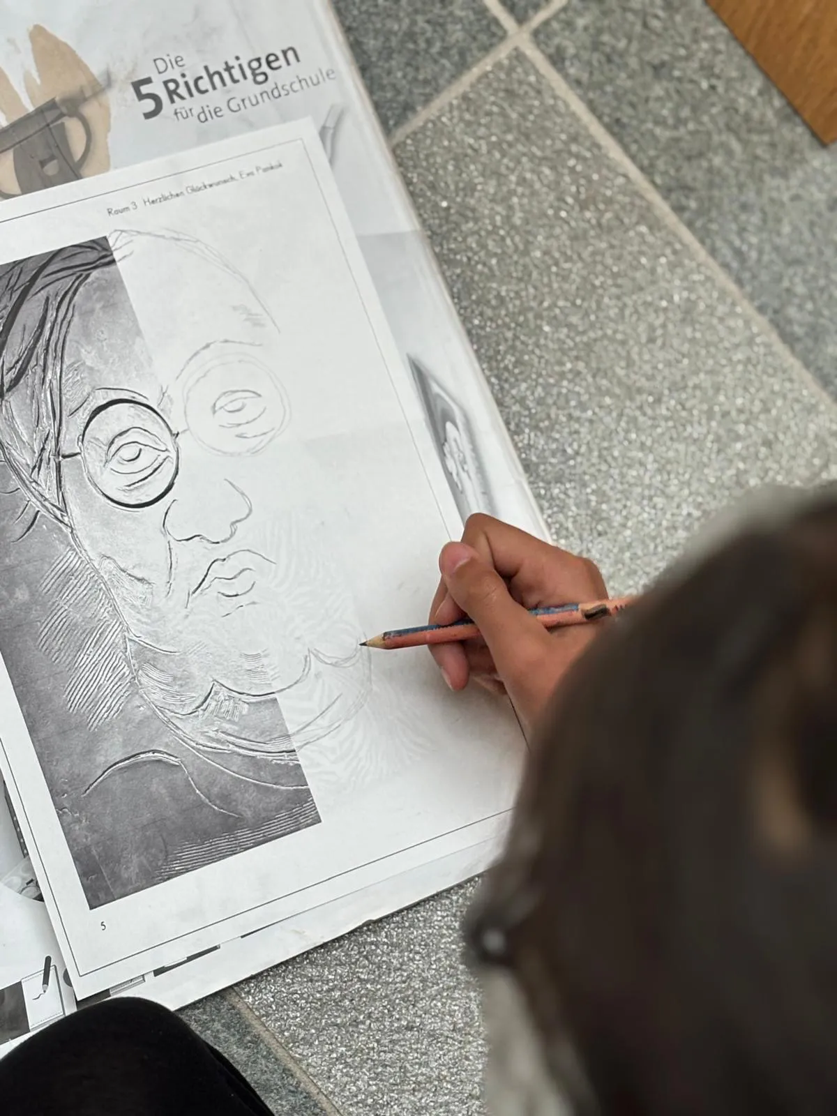 Ein Kind zeichnet ein Porträt von Otto Pankok nach, Vorlage liegt auf dem Boden. Ein Kind zeichnet ein Porträt von Otto Pankok nach, Vorlage liegt auf dem Boden.