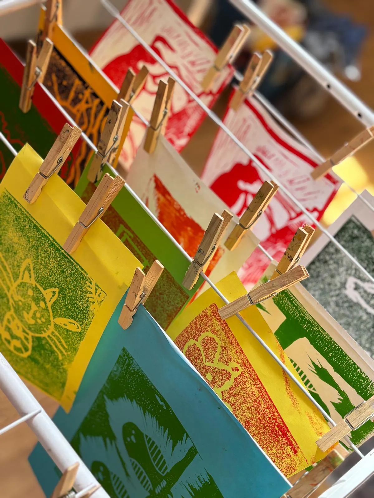 Farbenfrohe Linoldrucke mit verschiedenen Motiven hängen mit Wäscheklammern an einer Leine zum Trocknen. Farbenfrohe Linoldrucke mit verschiedenen Motiven hängen mit Wäscheklammern an einer Leine zum Trocknen.